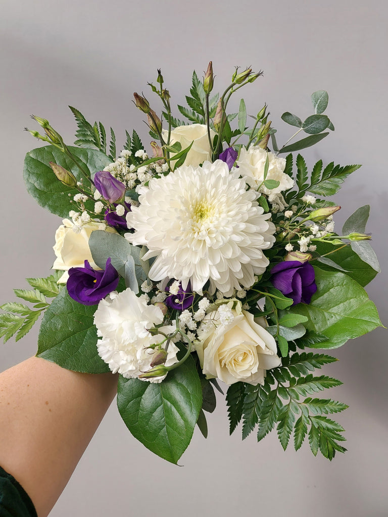 Kukkakimppu, jossa on valkoista krysanteemia, ruusua ja neilikkaa, sekä violettia eustomaa.