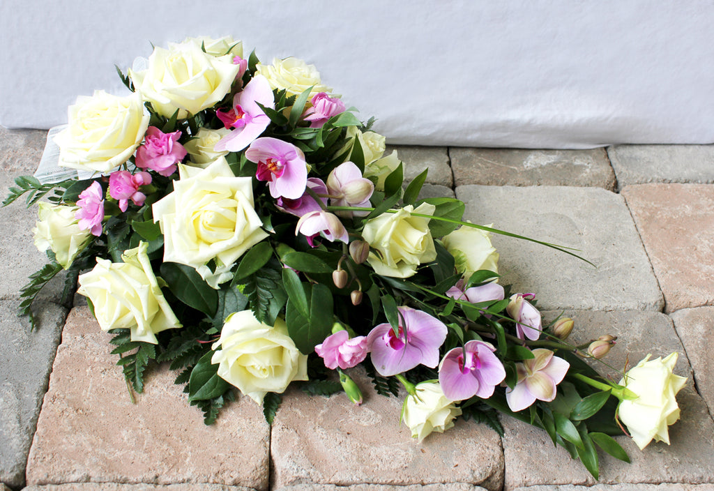 Kukkalaite hautajaisiin. Valkoista ruusua, vaaleanpunaista neilikkaa, vaaleanviolettia orkideaa.