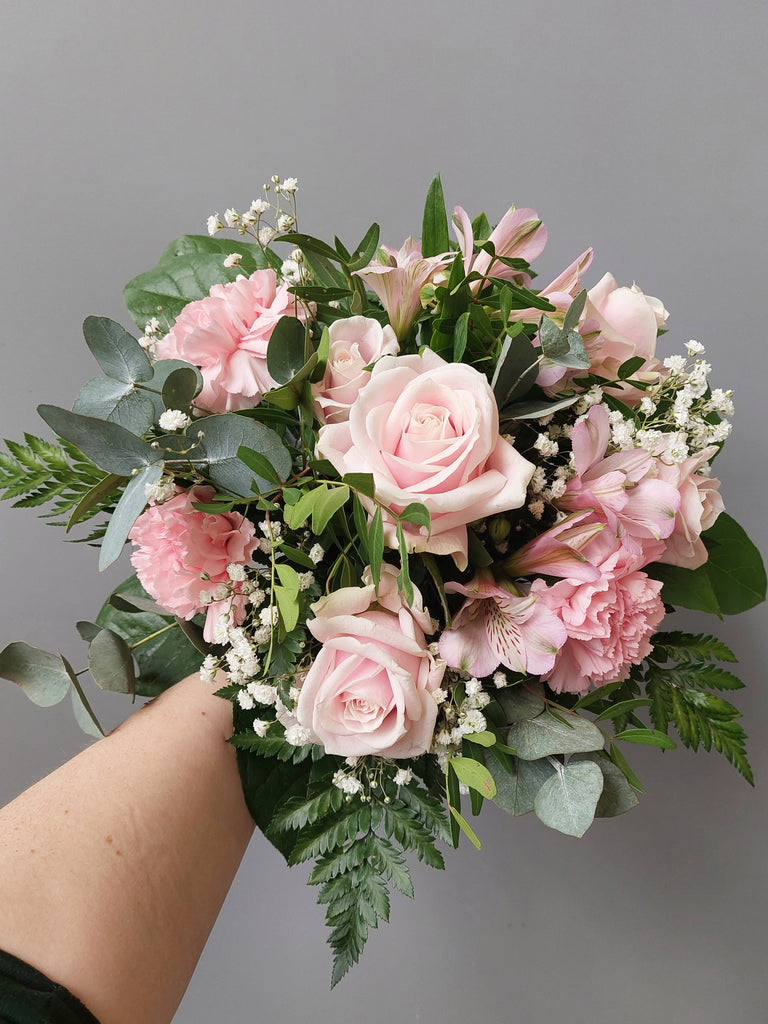 Kukkakimppu, jossa on vaaleanpunaista ruusua, neilikkaa ja inkaliljaa, sekä valkoista harsokukkaa.