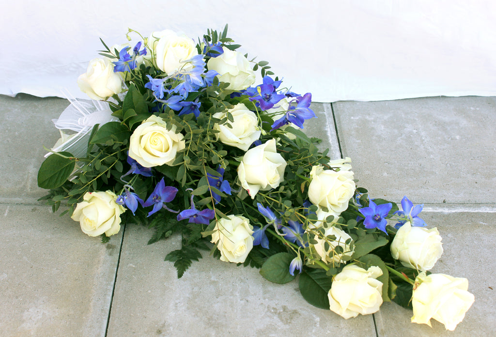 Kukkalaite hautajaisiin. Valkoista ruusua ja sinistä ritarinkannusta.