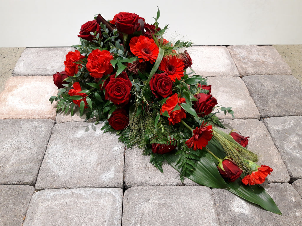 Kukkalaite hautajaisiin. Punaista ruusua, neilikkaa ja germiiniä.