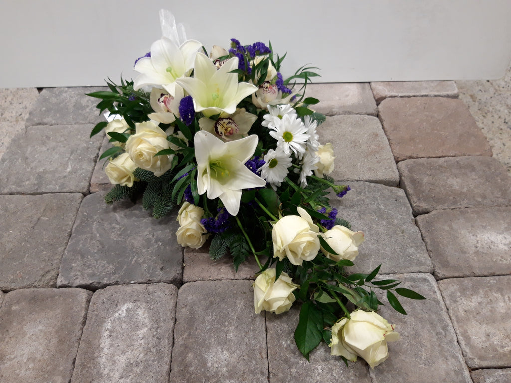 Kukkalaite hautajaisiin. Valkoliljaa, valkoista ruusua ja krysanteemia, orkideaa, sinistä ikiviuhkoa.